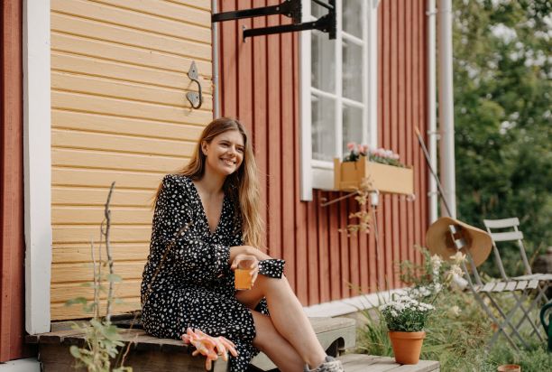Nainen istuu mökin portailla ja hymyilee.