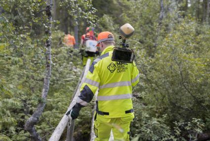 Joukko työasuisia maanmittareita kävelee metsässä.