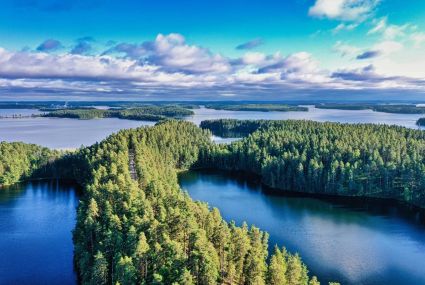 Aerial view of a lake landscape with blue water and islands covered in green forests. Clouds on the horizon.